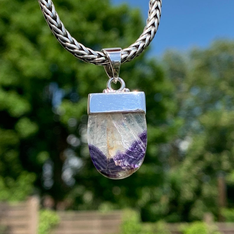 May include: A silver pendant featuring a purple and white fluorite stone. The pendant is on a silver chain.