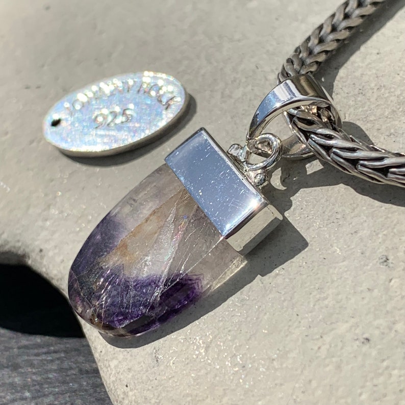 May include: A silver pendant with a purple and white crystal stone. The pendant is attached to a silver chain.