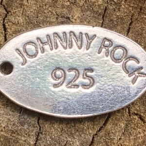 May include: A silver oval tag with the text "JOHNNY ROCK" and the number "925" engraved on it.