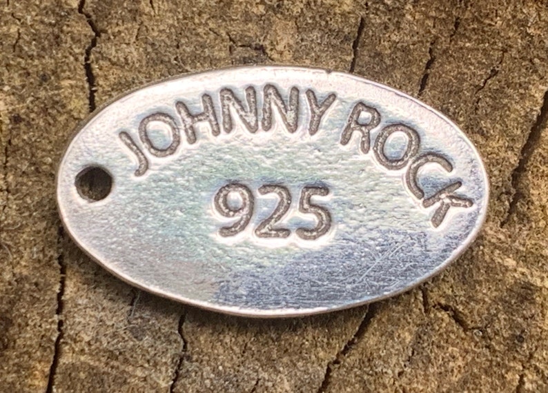 May include: A silver oval tag with the text "JOHNNY ROCK" and the number "925" engraved on it.