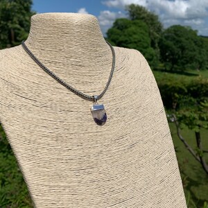May include: A silver chain necklace with a purple and white stone pendant.
