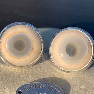 May include: A pair of silver cufflinks with a white agate stone inlay. The stone has a circular pattern with a darker center.