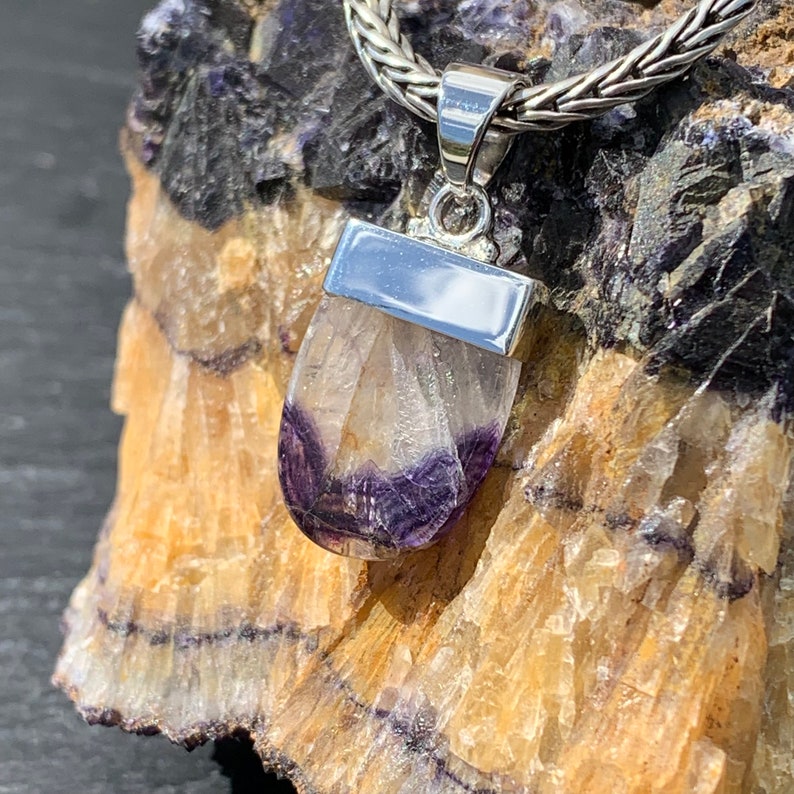 May include: A silver pendant featuring a clear, faceted fluorite stone with purple and white hues. The stone is set in a silver bezel and hangs from a silver chain.