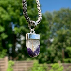 May include: A silver chain necklace with a pendant featuring a purple and white fluorite stone set in a silver bezel.