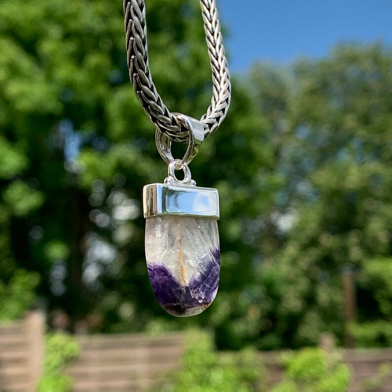 May include: A silver chain necklace with a pendant featuring a purple and white fluorite stone set in a silver bezel.