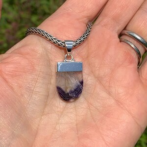 May include: A silver chain necklace with a pendant featuring a purple and white fluorite stone set in a silver bezel.
