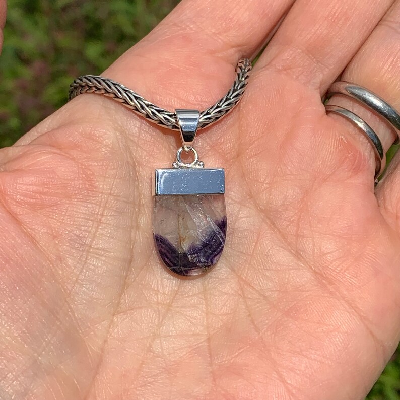 May include: A silver chain necklace with a pendant featuring a purple and white fluorite stone set in a silver bezel.