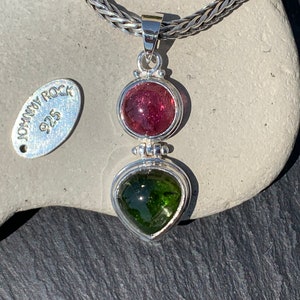 May include: A silver pendant with a green and pink gemstone. The pendant is on a silver chain and has a tag that says "Johnny Rock 925".