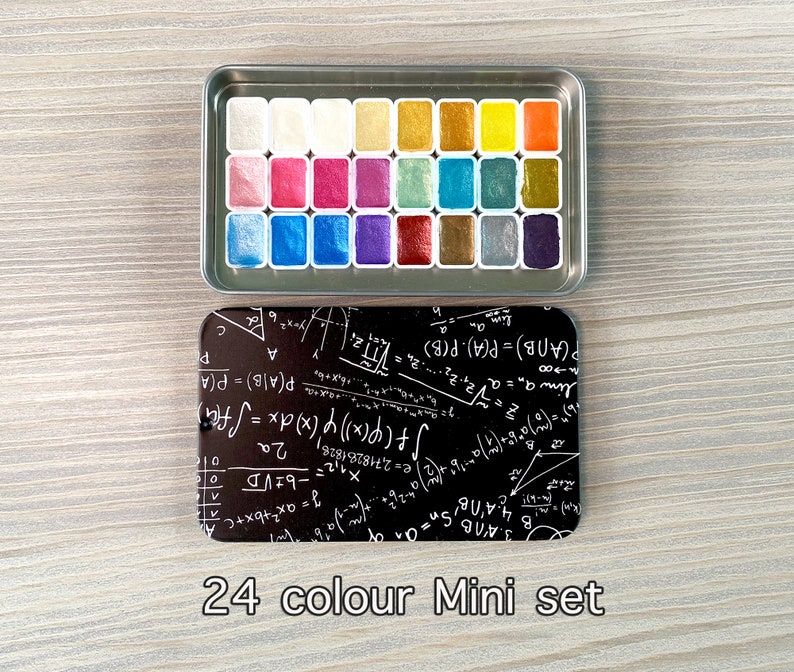 May include: A 24-color watercolor paint set in a silver metal case. The paint pans are arranged in a grid pattern and are filled with various colors, including gold, silver, blue, green, and purple. The case has a black background with white mathematical equations and formulas.