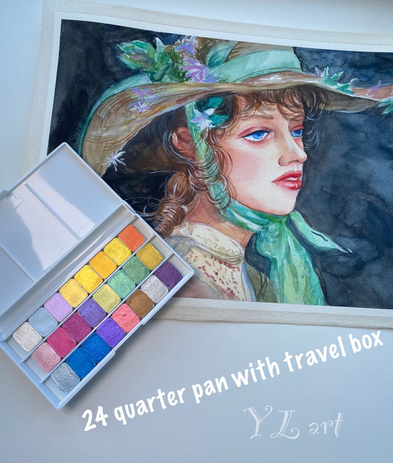 May include: A set of 24 watercolor paints in a travel box. The paints are arranged in a grid of 4 rows and 6 columns. The paints are a variety of colors, including silver, gold, pink, blue, green, and purple. The box is white with a silver trim. The text "24 quarter pan with travel box" is printed on the bottom of the image. The text "YL art" is printed in a cursive font on the bottom right of the image.