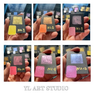 May include: Twelve small square samples of metallic paint in various colors, including gold, silver, pink, and blue. Each sample is labeled with a number from 1 to 12. The samples are arranged in two rows of six, and the text "YL ART STUDIO" is printed below the samples.