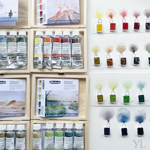 Puede incluir: Un juego de 10 tubos de pintura acuarela en una caja de madera. Los tubos están etiquetados con "BORADAM AQUARELL" y tienen una variedad de colores, incluyendo azul, verde, amarillo, naranja y rojo. Los tubos de pintura están dispuestos en dos filas de cinco. La caja de madera tiene una etiqueta que dice "NEW ADAM AQUARELL" y una imagen de un paisaje desértico. Los tubos de pintura están dispuestos en una caja de madera con una etiqueta que dice "NEW ADAM AQUARELL" y una imagen de un paisaje desértico.