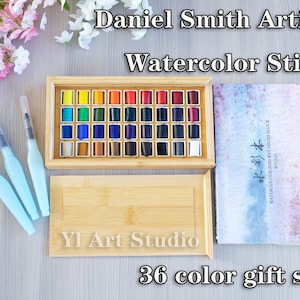 May include: A wooden box containing 36 watercolor sticks in a rainbow of colors. The box is labeled "Daniel Smith Artist Watercolor Stick" and "YI Art Studio". The text "36 color gift set" is printed below the box.