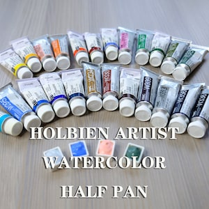 K&ouml;nnte beinhalten: Ein Satz Holbien Artist Aquarellfarben in Halb-Schalen. Die Tuben sind in einem Halbkreis auf einer Holzoberfl&auml;che angeordnet. Die Tuben sind mit der Farbnummer und dem Namen beschriftet. Die Farben umfassen W295, W234, W330, W339, W353, W356, W274, W338 und W055.