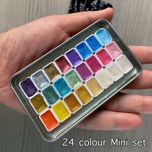 May include: A 24-color mini watercolor set in a silver metal tin. The set includes a variety of metallic and iridescent colors.