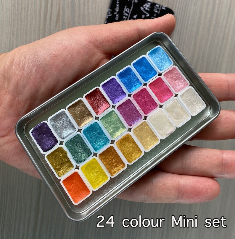 May include: A 24-color mini watercolor set in a silver metal tin. The set includes a variety of metallic and iridescent colors.
