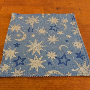 Puede incluir: Un mantel individual de tela azul con un patrón de estrellas blancas y medias lunas.