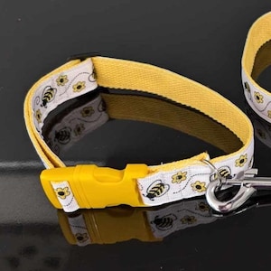 Peut inclure: Collier pour chien jaune et blanc orné d'un motif d'abeilles et de fleurs. Le collier est doté d'une boucle en plastique jaune et d'un attache-laisse en métal argenté. Fabriqué en tissu résistant.