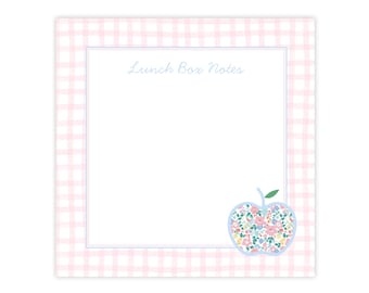 May include: A square notepad with a pink and white gingham border. The notepad has a light blue border around the blank writing space. The words "Lunch Box Notes" are written in light blue script. A floral apple graphic is in the bottom right corner.