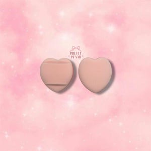 May include: Two pink heart-shaped makeup sponges. One sponge has a flat surface and the other has a rounded surface.