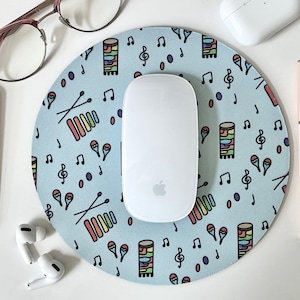 May include: A blue round mouse pad with a colorful musical instrument pattern. The pattern includes xylophones, maracas, and musical notes. A white wireless mouse is on top of the mouse pad.