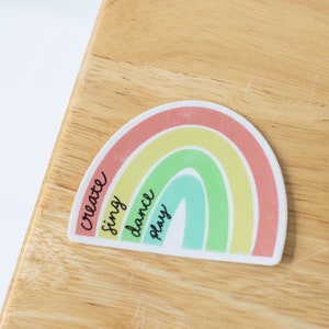 Puede incluir: Una pegatina de arcoíris con las palabras "create", "sing", "dance" y "play" escritas en ella.