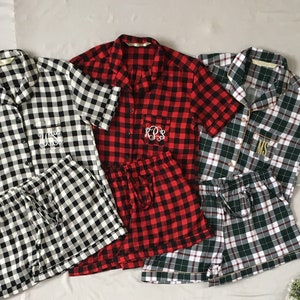 Puede incluir: Tres conjuntos de pijamas con mangas cortas y pantalones cortos a juego. Las pijamas están hechas de tela a cuadros en blanco y negro, rojo y negro, y verde y blanco.