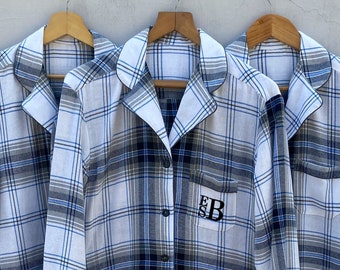 May include: Three white and blue plaid shirts with long sleeves and button-down collars. The middle shirt has the initials "EB" embroidered on the left chest pocket.
