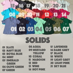 Pode incluir: Cole&ccedil;&atilde;o de camisas de pijama de manga curta em v&aacute;rias cores s&oacute;lidas, incluindo ard&oacute;sia, azul marinho e &aacute;gua. Cada camisa &eacute; numerada e rotulada com o nome da cor. A palavra "SOLIDS" &eacute; exibida abaixo.