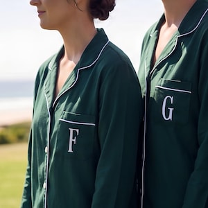 May include: Three dark green long-sleeved button-down pajama shirts with white piping along the collar and front placket. Each shirt features a single chest pocket embroidered with a large white letter, specifically F, G, and H respectively.