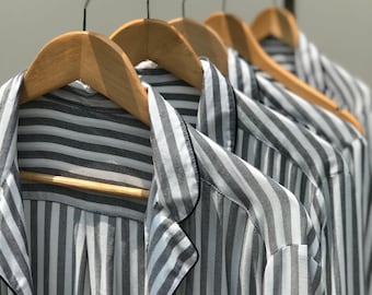 May include: Close-up of striped shirts hanging on wooden hangers. The shirts are black and white with a subtle sheen.