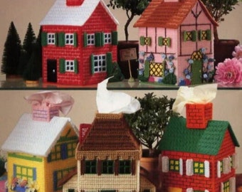 May include: Five different tissue box covers in the shape of houses. The houses are made of plastic canvas and are decorated with yarn. The houses are red, pink, yellow, green, and brown. The houses are all different sizes and shapes.