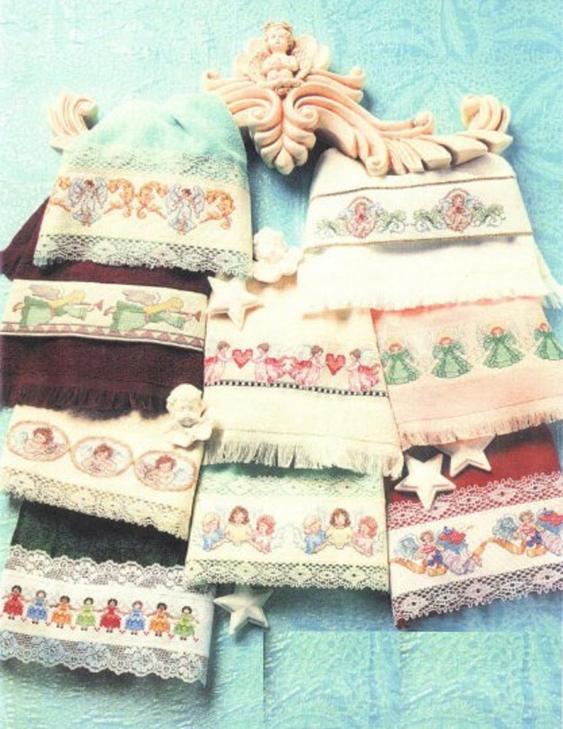 Op de afbeelding: Een verzameling van acht geborduurde handdoeken met engelen en harten. De handdoeken worden getoond op een decoratieve handdoekhouder met een witte achtergrond.