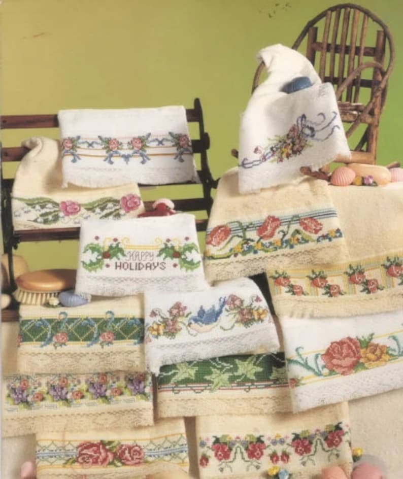 May include: A collection of embroidered hand towels featuring various floral and festive designs. The towels are displayed on a wooden rack and a chair. The designs include flowers, birds, and the phrase "Happy Holidays".