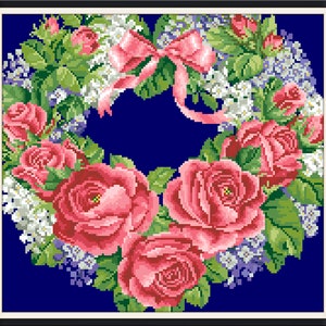May include: A heart-shaped wreath of pink roses and white flowers with a pink bow on a dark blue background.