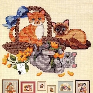 May include: Cross stitch pattern featuring three cats in a basket with flowers. The pattern includes a tabby cat, a Siamese cat, and a gray tabby cat. The pattern is framed and includes a small tag with the text "0516 7351 17".
