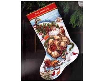 May include: A white Christmas stocking with a red cuff and the name "Nicholas" embroidered on it. The stocking features a winter scene with Santa Claus carrying a Christmas tree and a sled with presents. There are also red cardinals in the scene.