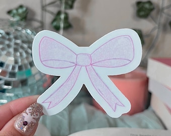 May include: A white sticker with a pink bow drawn on it. The bow is drawn with a light pink color and has a textured look.