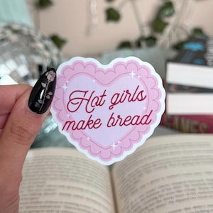 Könnte beinhalten: Ein rosa herzförmiger Aufkleber mit weißem Rand und einem gewellten Rand. Der Aufkleber hat einen weißen Hintergrund mit rosa Glitzer und den Text "Hot girls make bread" in roter Kursivschrift.