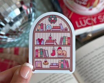 May include: A sticker featuring a bookshelf design with Christmas-themed decorations. The sticker includes a wreath, wrapped gifts, a candy cane, a stocking, and a cat wearing a Santa hat. Bookshelves are filled with colorful books.
