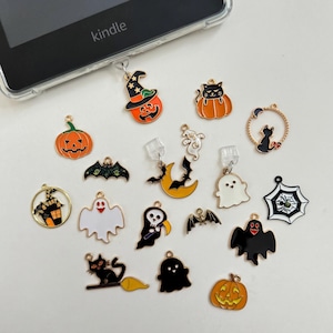 May include: A selection of Halloween-themed charms featuring pumpkins, bats, ghosts, and black cats. The charms are brightly coloured with black, orange, white, and green details. The word "kindle" is visible on the top of the image.