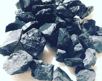 Può includere: Una collezione di pietre grezze di ossidiana nera. Le pietre sono di varie dimensioni e forme, con una texture ruvida e naturale.