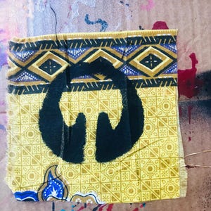 May include: A black silhouette of a person with arms raised is stenciled onto a yellow fabric with a blue and gold geometric pattern.