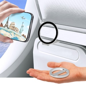 May include: A silver phone ring holder and a black and silver phone lens protector are displayed. A smartphone shows a world travel scene with the Eiffel Tower and Statue of Liberty. The items are shown against a white background.