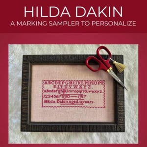May include: A framed embroidery sampler with the text "HILDA DAKIN" and "A MARKING SAMPLER TO PERSONALIZE". The sampler features an alphabet, numbers, and the text "Hilda Dakin aged 2 years". Red scissors with a gold tassel are on the frame.