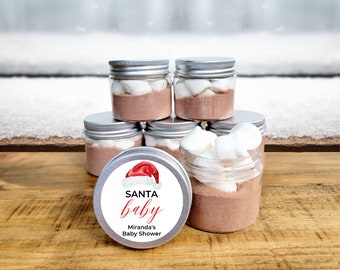May include: A set of six clear glass jars with silver lids filled with hot chocolate mix and marshmallows. The jars have a white label with a red Santa hat and the text "SANTA baby Miranda's Baby Shower".