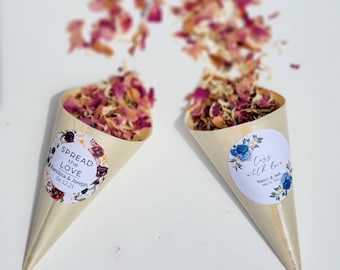 May include: Two wooden cones filled with dried flower petals. The cones have labels with wedding-themed text. One cone says "Spread the Love" with the names Karolina & Joseph and the date 06.12.21. The other cone says "Loss with love" with the names Nancy & Jack and the date May 10, 2021.