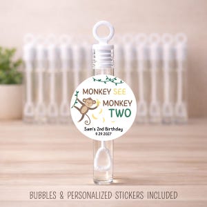 May include: Clear bubble wand with a white cap and a round sticker. The sticker reads "MONKEY SEE MONKEY TWO" with a cartoon monkey and bananas. Text at the bottom says "Sam's 2nd Birthday 9.29.2027". The bottom text says "BUBBLES & PERSONALIZED STICKERS INCLUDED".