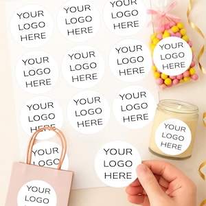 May include: Custom stickers with the text "YOUR LOGO HERE" printed on white circles. The image includes stickers on a sheet, a gift bag, a candle, and a bag of candy. Sizes available: 1", 1.5", 1.75", 2", 2.25", and 3.33".