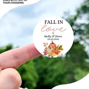 May include: Fall in love themed circle sticker with a watercolor illustration of pumpkins and leaves. The sticker says "Fall in love" with a heart and "Molly & Drew 09.29.2026". The sticker is available in sizes 1 inch, 1.5 inch, 1.75 inch, 2 inch, 2.25 inch, and 3.33 inch. The sticker pictured is 2 inches.